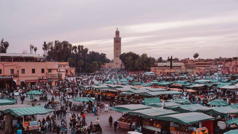 A realistic scene inside a traditional Marrakech artisan workshop where a craftsman shapes copper by hand, warm daylight entering through a small window, tools and handmade pieces around the room, reflecting the living heritage and human craftsmanship of the Red City.