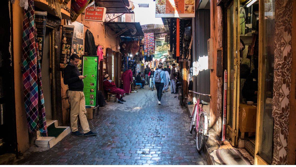 Narrow alley in the old medina of Marrakech showing everyday life among traditional shops, local residents, and visitors