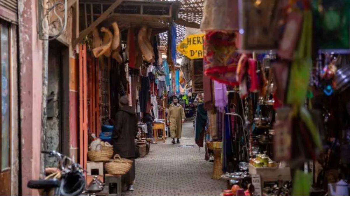 Traditional souk alley in Marrakech with local vendors, hanging crafts, and a man walking through the narrow market street.