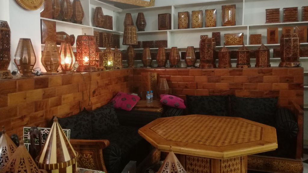 Handcrafted Moroccan lanterns and carved wooden furniture inside a traditional Essaouira artisan shop, glowing with warm ambient light.