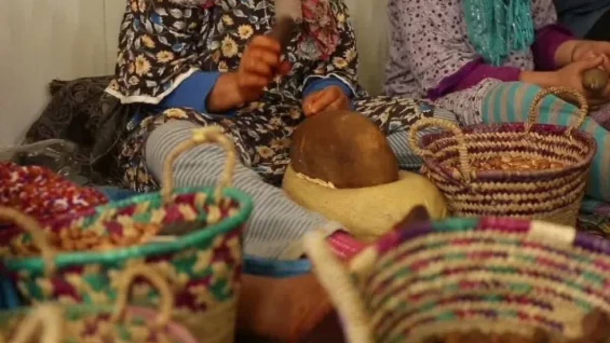 Local women hand-cracking argan nuts in a traditional cooperative workshop near Essaouira, using stones and natural fiber baskets, highlighting Moroccan ancestral craftsmanship and communal wellness traditions.