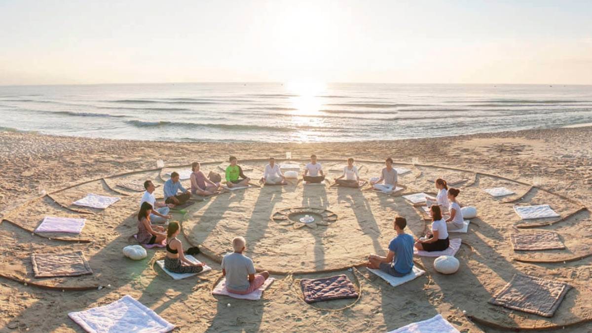 Group meditation circle on Essaouira beach at sunset, reflecting wellness travel, mindfulness, and cultural harmony by the Atlantic Ocean.
