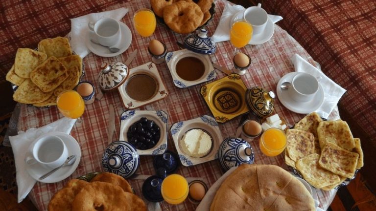 Traditional Moroccan breakfast table with msemen, khobz bread, olives, eggs, fresh orange juice, olive oil, Amlou, Argan oil , jben and Moroccan tea set, representing cultural food rituals and mindful living.